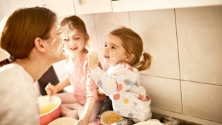 Two girls sitting on a kitchen countertop covering their mom in flour