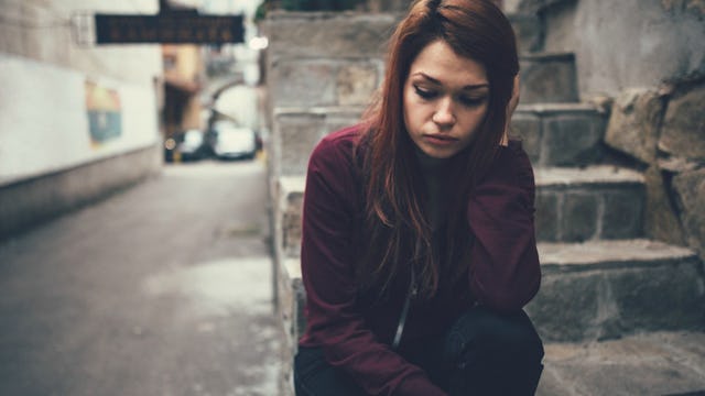 A girl suffering from panic attacks sitting alone on the stairs looking sad.