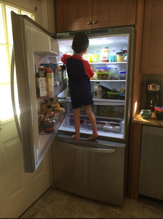 A boy with ADHD climbing and standing in an open fridge and taking food out