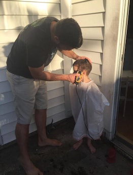 A dad doing his son's haircut in front of the house 