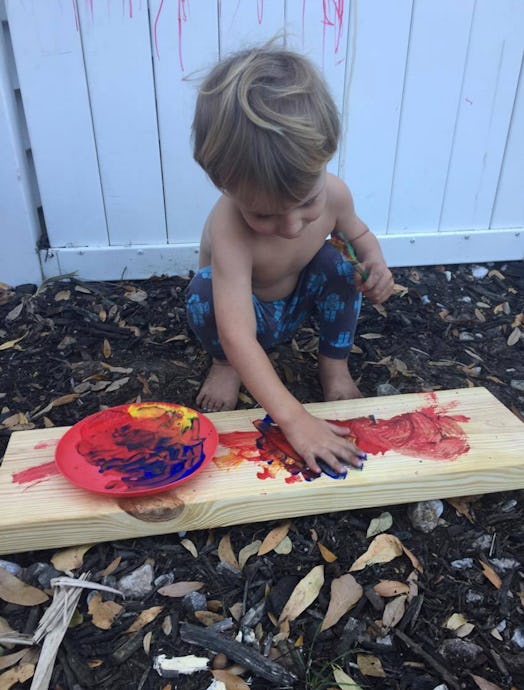 A little boy painting on the wood with his hands 