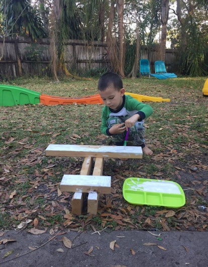 A boy painting wood blocks outside