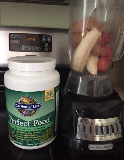 A bottle of 'Perfect Food' supplements next to a blender filled with fruits.