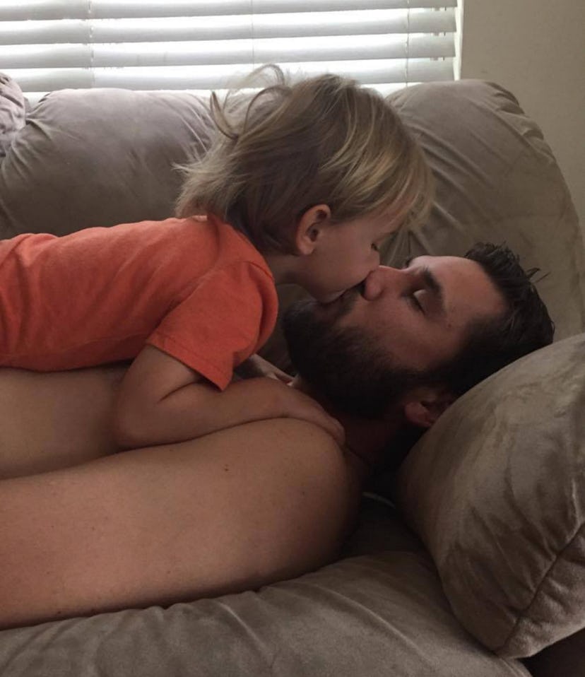 A child kissing his dad  while he is lying on the couch 