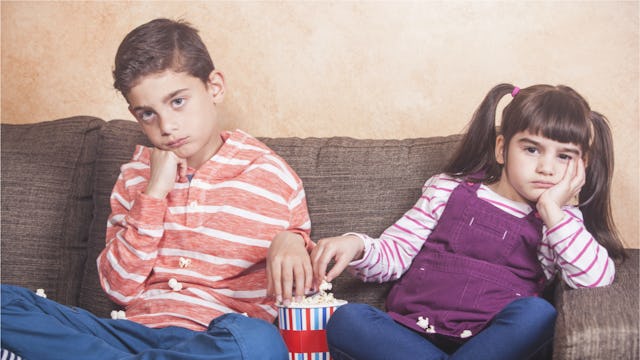 Young boy and girl sitting on a sofa looking bored.