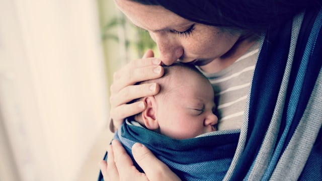 A mother holding her baby on her chest and kissing his head