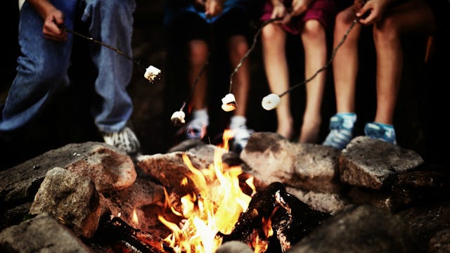 Kids gathered around the campfire holding sticks with marshmallows on top at a sleepaway camp