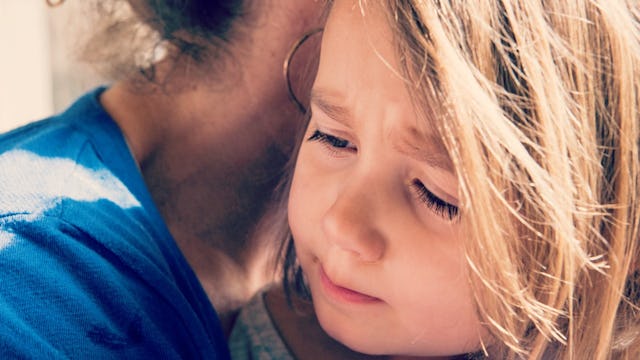 Little girl with special needs looking down in her mother's arms