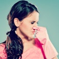 A woman holding her nose with her left hand due to stink and an air freshener in her right hand