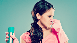 A woman holding her nose with her left hand due to stink and an air freshener in her right hand