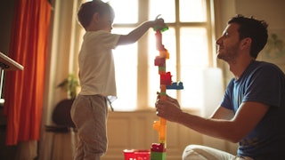 A boy playing with building blocks with his dad who also has a micromanaging mom