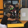 A disabled kid in a wheelchair entering a school bus on a disability specialized back door