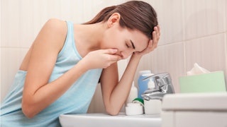 A girl suffering from emetophobia, leaning on the sink in the bathroom while covering her mouth