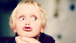 A difficult-to-control child making a duck face while their hands are underneath their chin with a b...