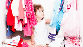 A girl in a white dress sitting in wardrobe surrounded by clothes