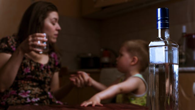 A mother with an alcohol addiction talking to her child with a bottle on a table in front of them