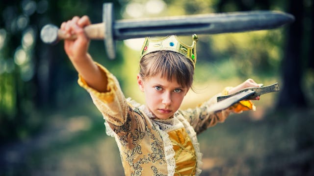 A girl dressed in a golden princess dress with a crown on her head and a sword symbolizing a new kin...