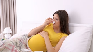 pregnant woman, woman touching pregnant belly, pregnant woman wiping nose, pregnant woman stuffy nos...