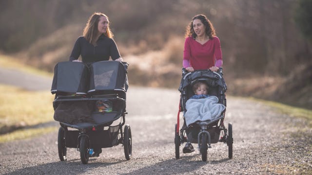 Two women wearing black and pink outfits pushing baby carts with children with special needs