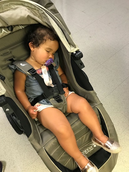 A little girl sleeping in a trolley with a pacifier in her mouth 