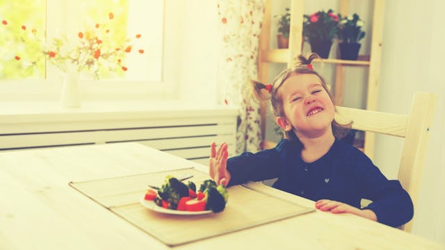 A girl with pigtails in a black long-sleeved shirt sitting by a white dining table with a rejecting ...