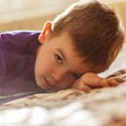 A strong-willed toddler in a purple t-shirt laying on the bed