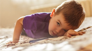 A strong-willed toddler in a purple t-shirt laying on the bed