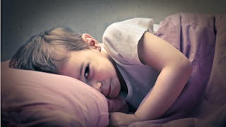 A boy in a grey T-shirt lying on a bed on a red pillow covered with a grey duvet