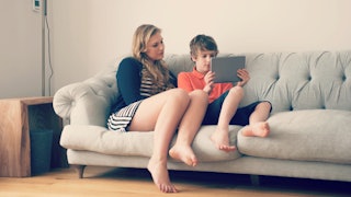 A mother and her son sitting on a beige couch while looking at a tablet
