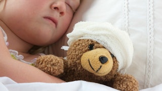 A child who is prone to seizures hugging his teddy bear with bandage wrapped over its head while sle...
