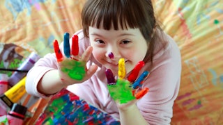 A girl with Down syndrome showing off her painted hands while smiling