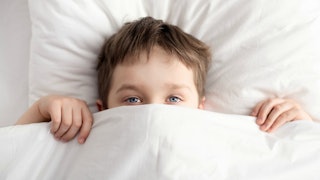 A child hiding half of his face under bedsheets after he ate too many beans for dinner