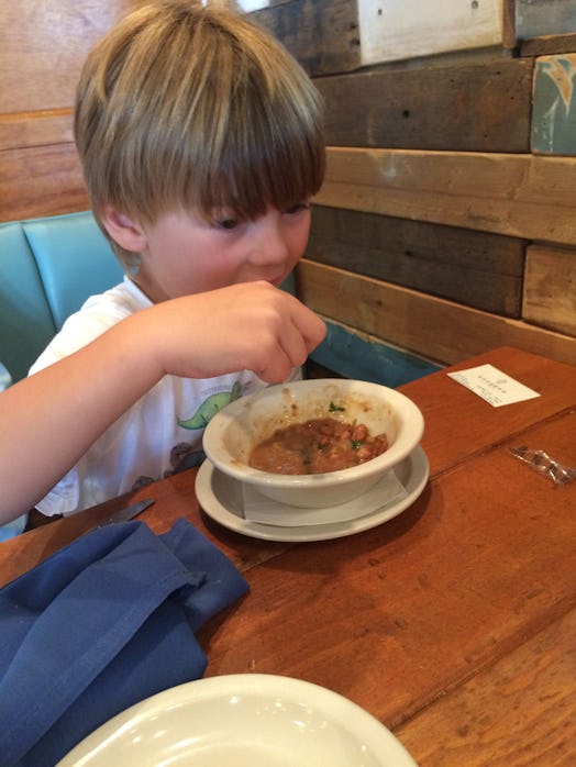A child sitting in a restaurant eating beans.