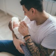 Tattooed man sitting and holding a baby girl, looking at her 