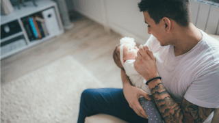 Tattooed man sitting and holding a baby girl, looking at her 