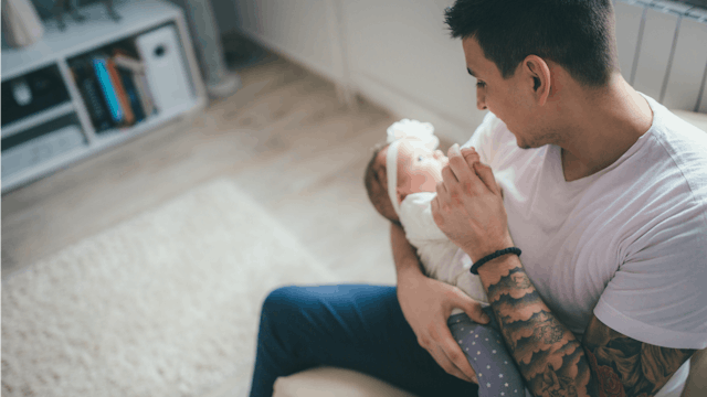 Tattooed man sitting and holding a baby girl, looking at her
