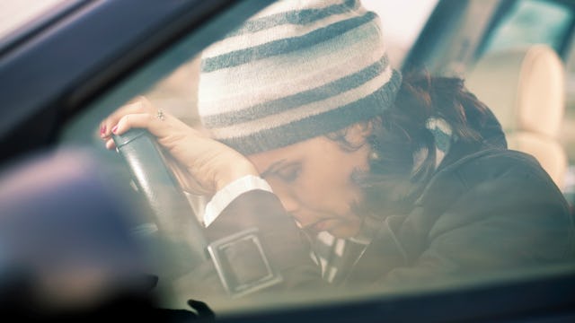A woman wearing a black and white striped wool cap leaning her head on the steering wheel in the car...
