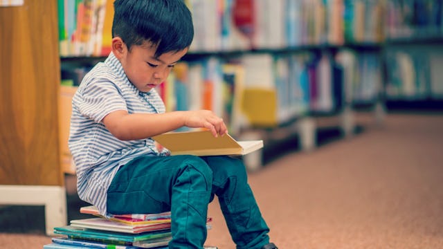 5-Year-Old kid sitting in the library and reading a book