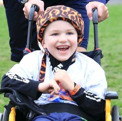 A smiling kid in a wheelchair wearing a black and white shirt and a black hat with red flames