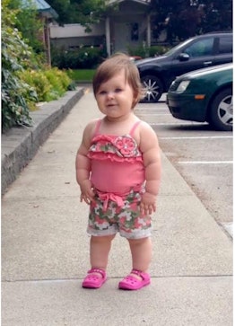 A toddler standing on the sidewalk in a pink top, floral shorts and pink crocs 