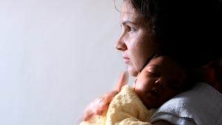 A mom holding her newborn baby on her chest while looking off into the distance