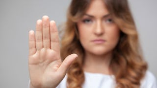 The palm of a brunette woman's hand in the front and her face in the background slightly blurred wit...