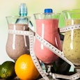 Three smoothies wrapped with measuring tape and fruits around them as a symbol for a diet for a beac...