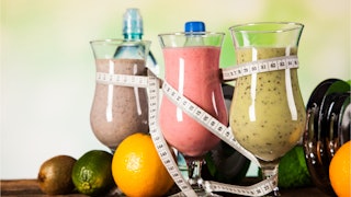 Three smoothies wrapped with measuring tape and fruits around them as a symbol for a diet for a beac...