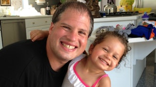 An uncle, and his niece, little curly-haired girl in a white polka-dot dress, hugging and smiling to...