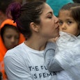 A mother in a white shirt with the print 'The future is female' holding and kissing her daughter in ...