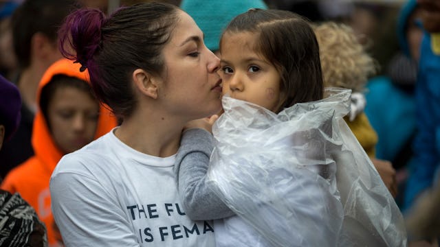 A mother in a white shirt with the print 'The future is female' holding and kissing her daughter in ...