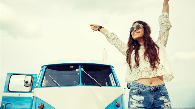 A 'free spirit' young happy girl with her hands up in the air, standing in front of a white-blue va...