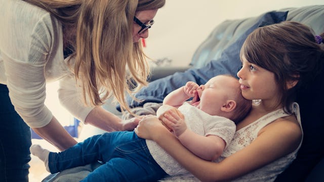 A mother leaning towards a smiling girl who's holding her baby sibling in her lap