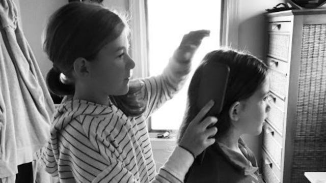 A girl styling her best friend's hair while standing behind in black and white